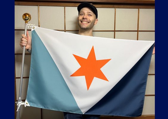 A man smiles while posing for a photo with the City of Syracuse flag.