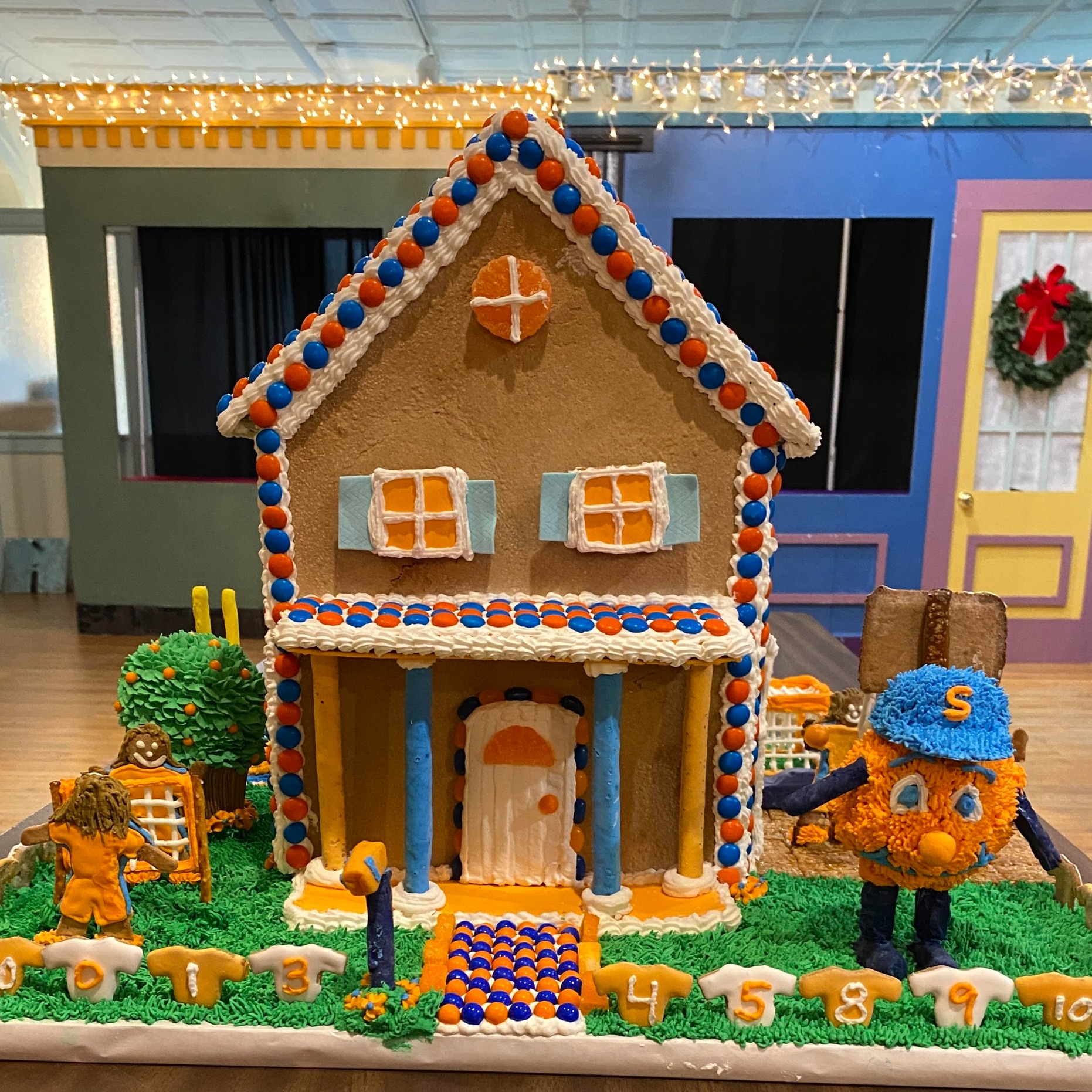 Gingerbread house decorated with orange and blue accents with an otto the orange in the front yard.