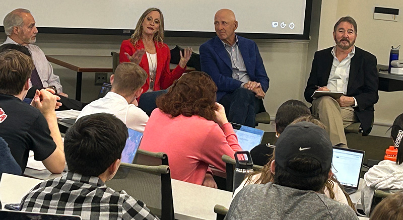 Michael Veley, Danielle Cantor, David Falk and Dennis Deninger sit in front of a crowd of students at a Falk College lecture