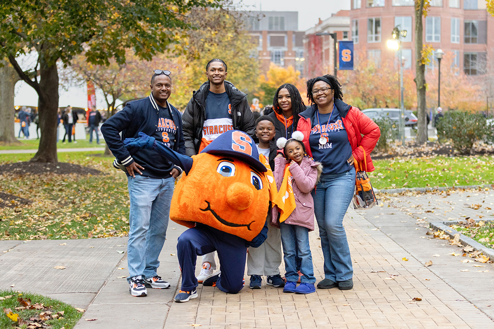 A family of six individuals poses with Otto on the Quad during family weekend