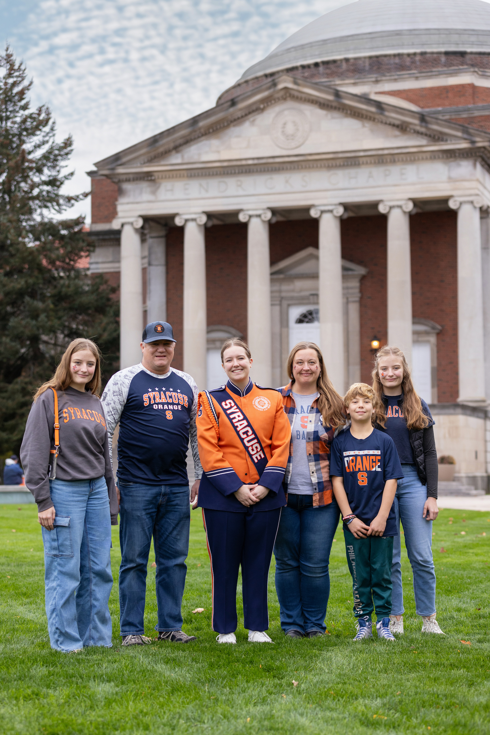 A family of six individuals pose together outside of Hendricks Chapel during the Family Weekend tailgate