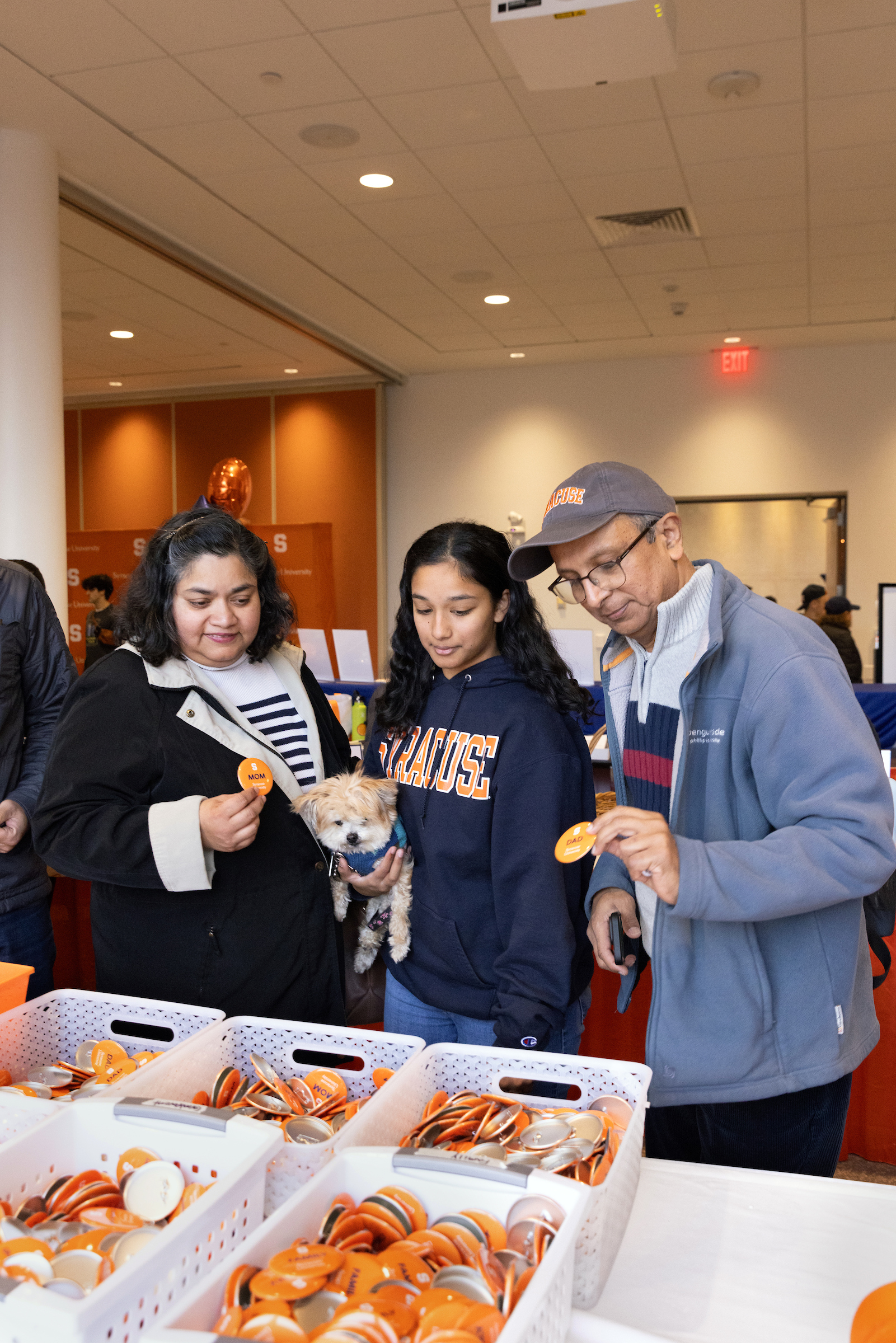 A group of three people pick out Orange buttons to wear at the Family Weekend welcome center