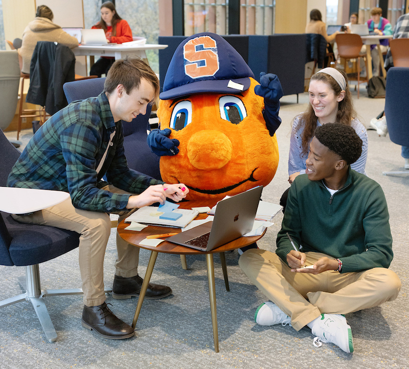 Otto the orange and three other students gathered around a table studying.