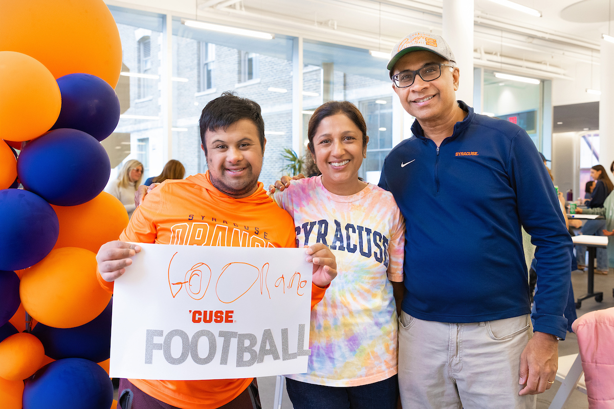 Three individuals in Syracuse gear with one holding up a sign that says "Go Orange Cuse Football"