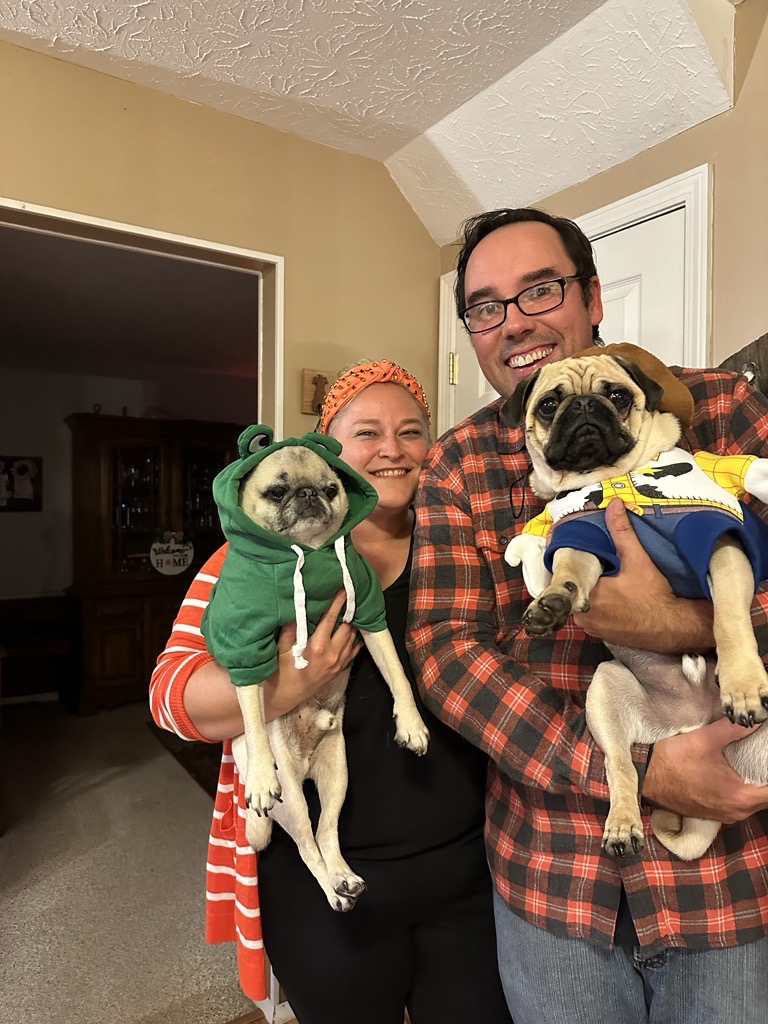 Two people, each holding a dog wearing a Halloween costume