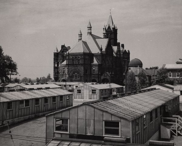 Black and white photo of long temporary buildings next to Crouse College.