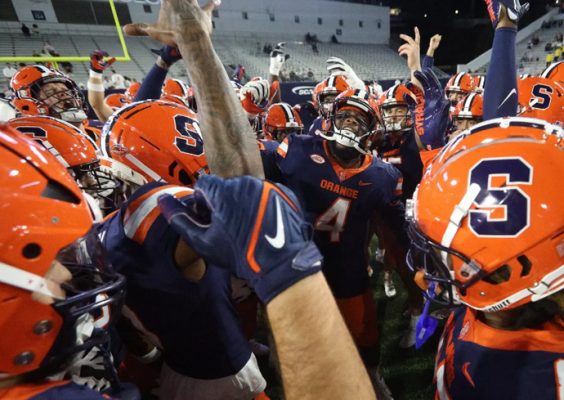 Student athletes on the Syracuse University football team put their hands in during a team huddle.