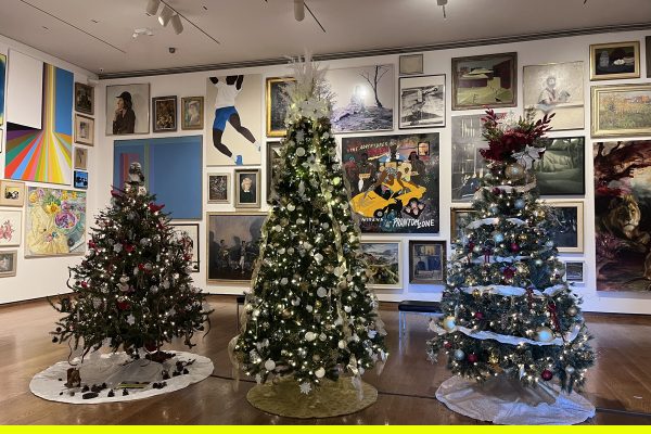 Three christmas trees decorated in a room filled with art on the wall. 