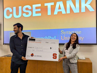 A man and a woman hold up a giant check during the 'Cuse Tank entrepreneurial competition.