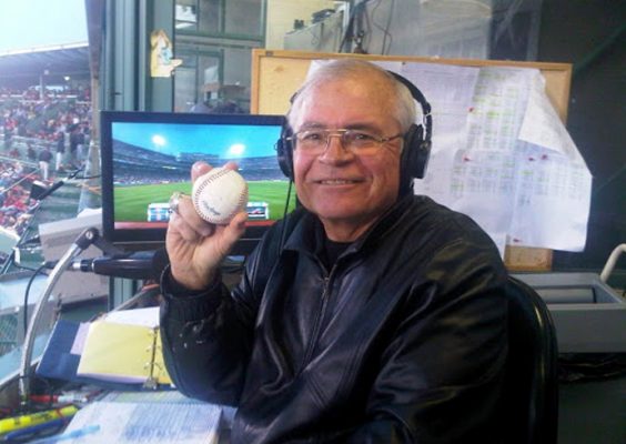 A man in a radio broadcast booth holding up a baseball.