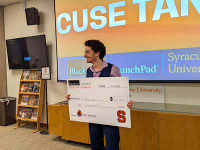 A man holds up a giant check after winning the 'Cuse Tank entrepreneurial competition. 
