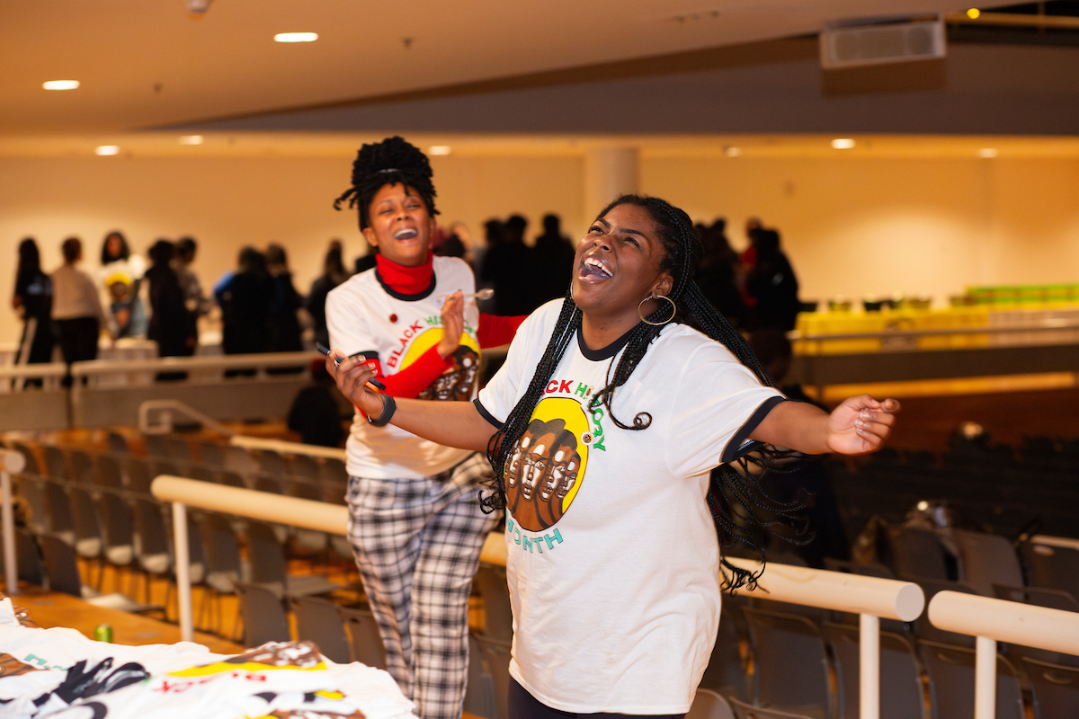 Two individuals in Black History Month t-shirts look joyful at the Black HIstory Month kickoff celebration