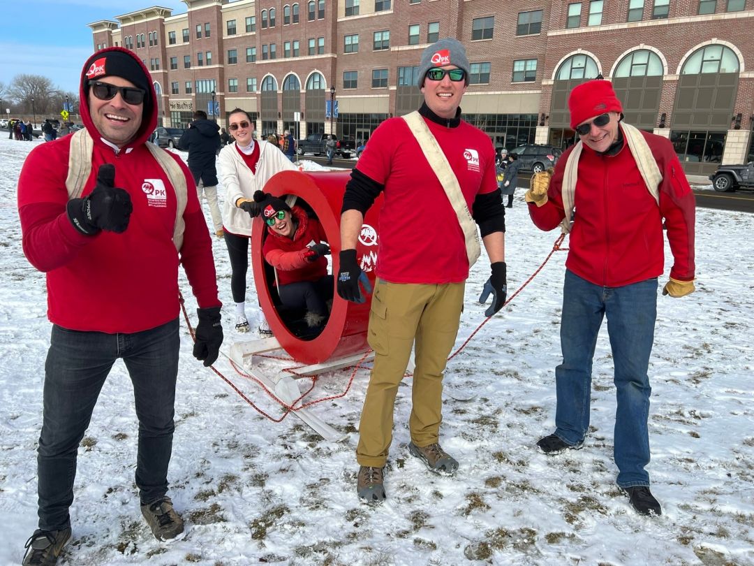 Five individuals wearing red shirts pulling someone in a sled