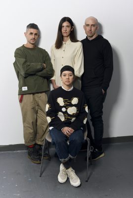 four individuals pose for a portrait against a white wall