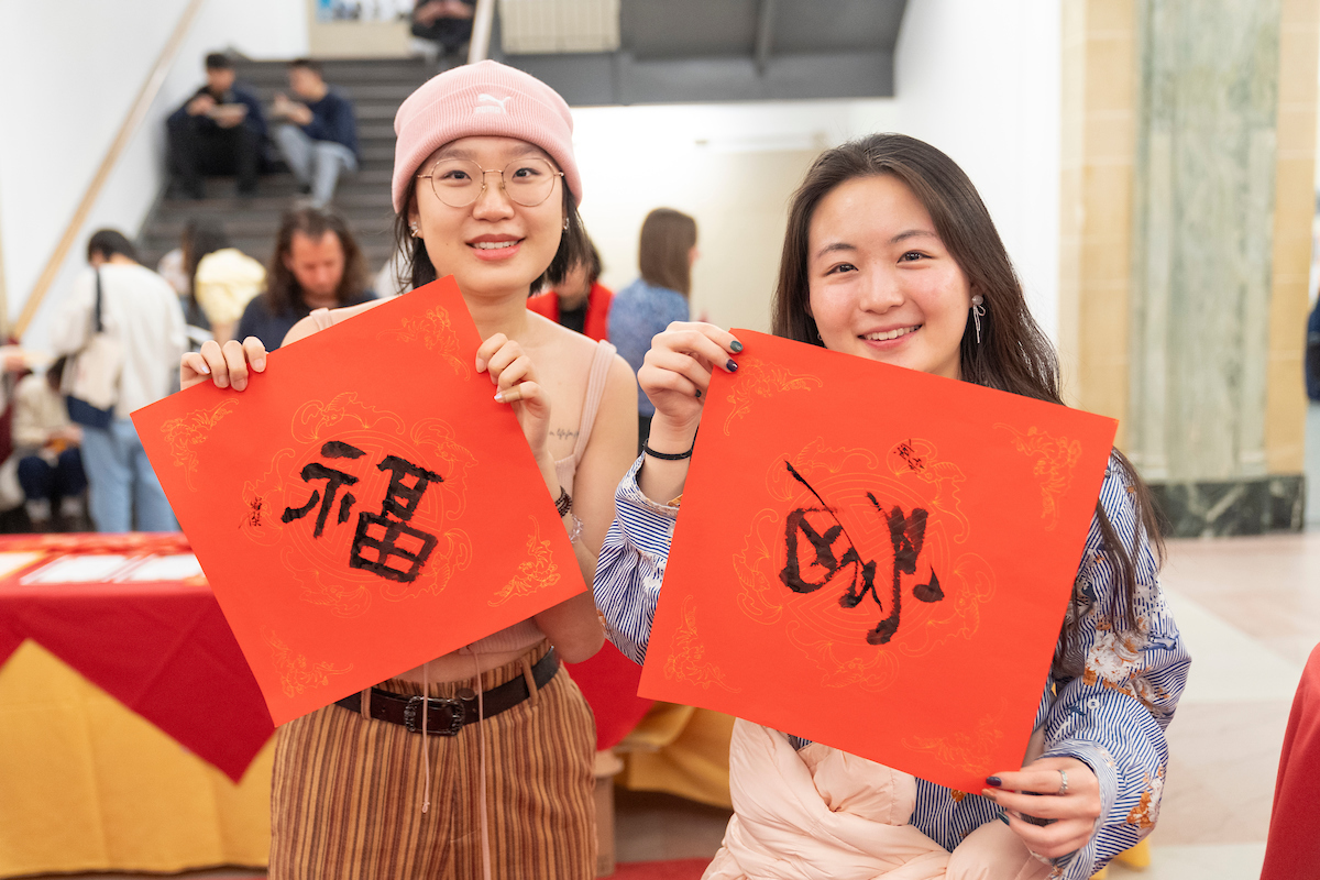 Two students holding up pieces of red paper with Chinese writing on them.