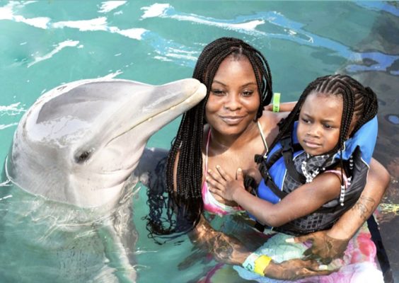 A woman and her daughter pose for a photo alongside a dolphin.