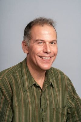 Headshot of man in green colored shirt smiling