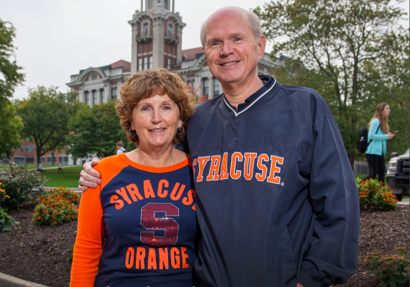 Two people wearing Syracuse clothing standing together on the promenade