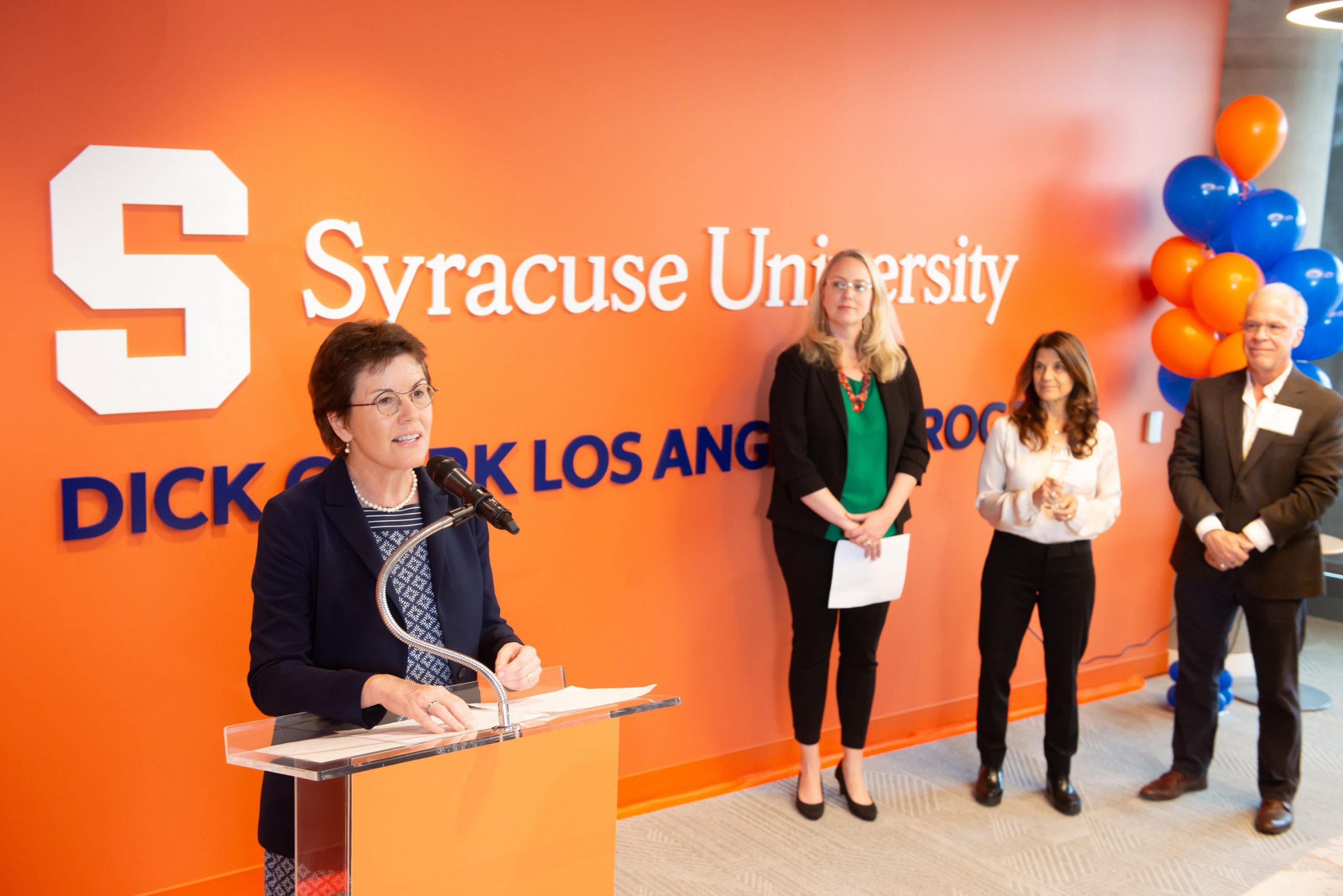 person speaking at podium with three people standing behind