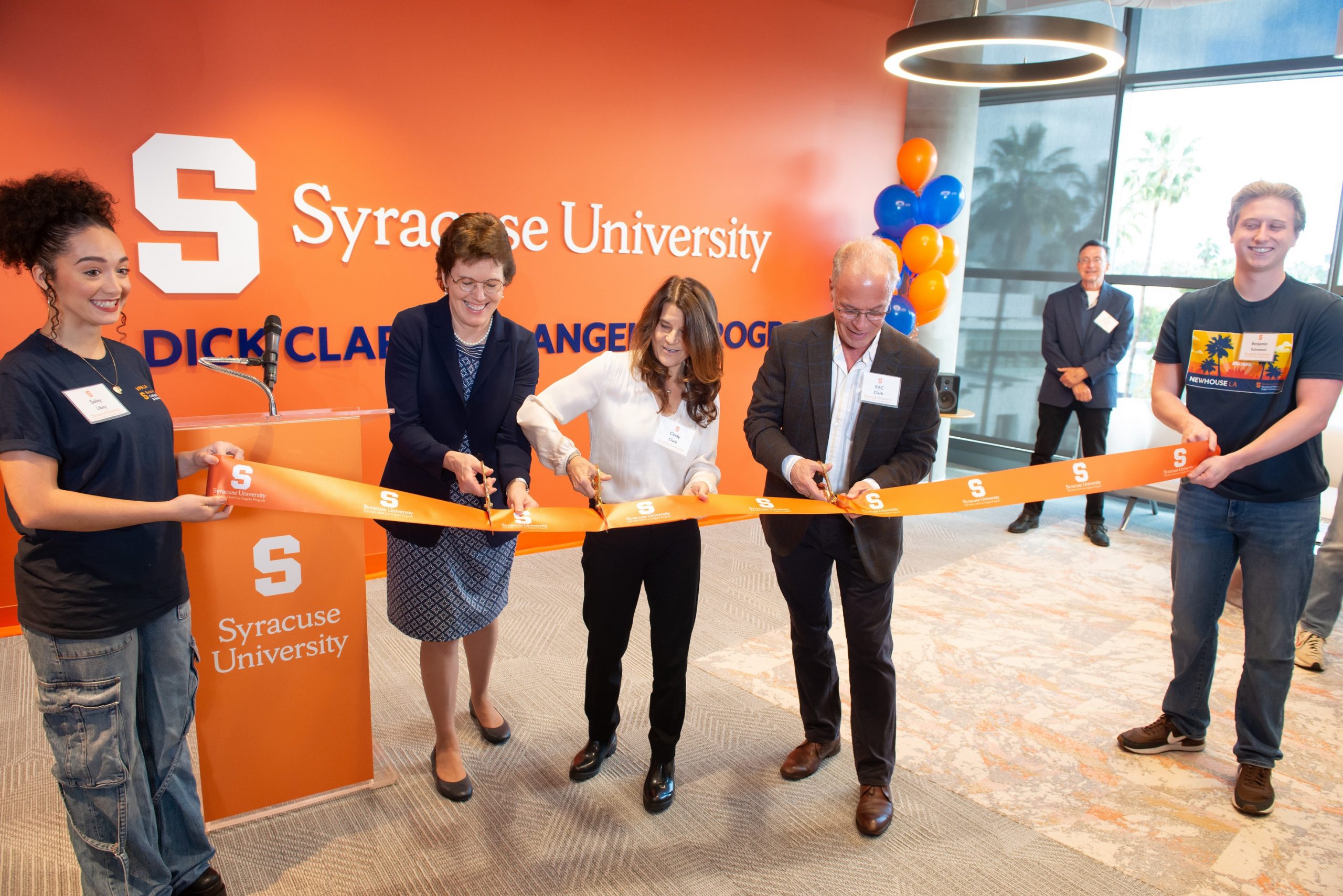 three people cutting ribbon, with two people holding ribbon at ends