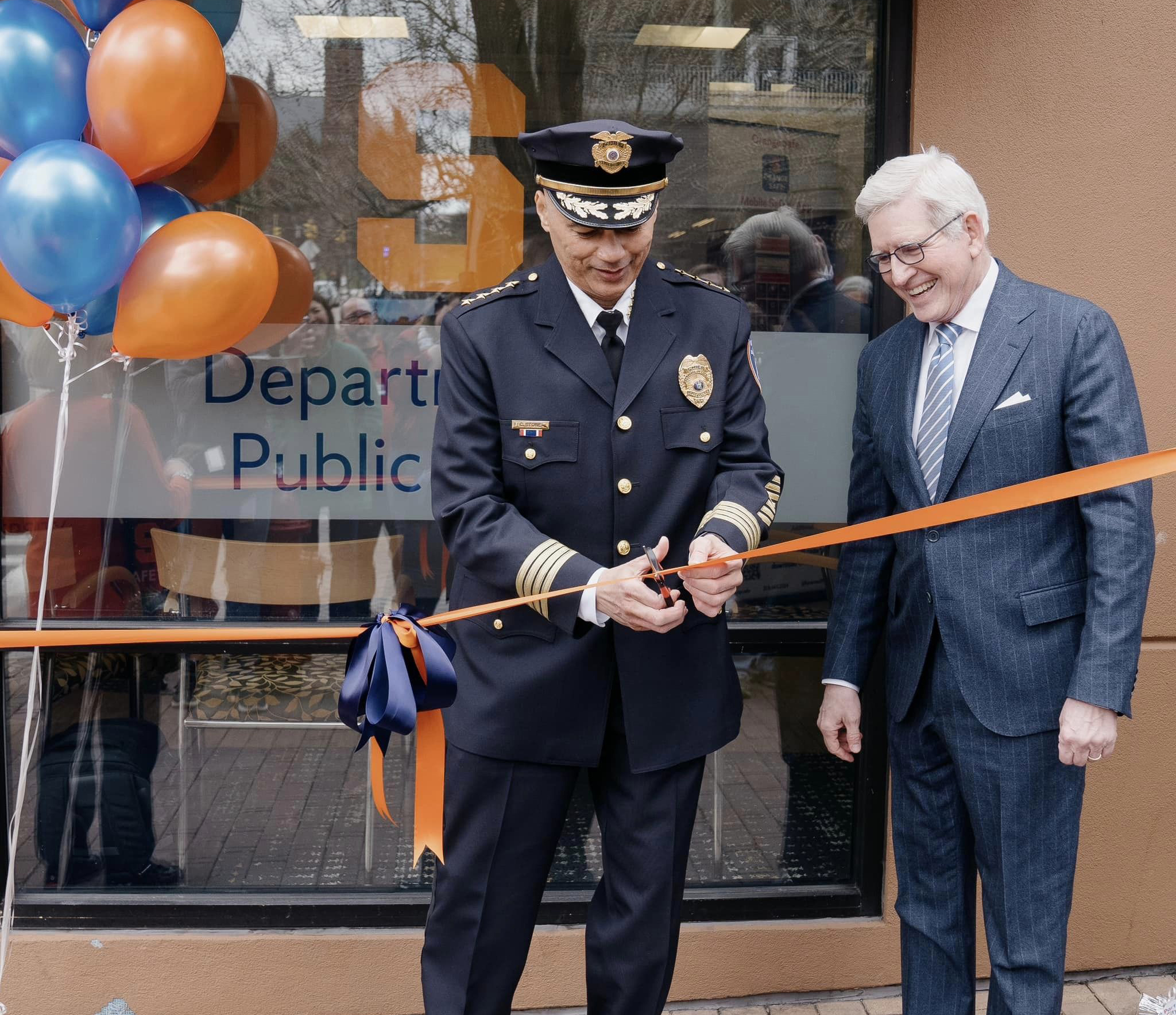 Man in police uniform cutting a ribbon with another man standing next to him. 