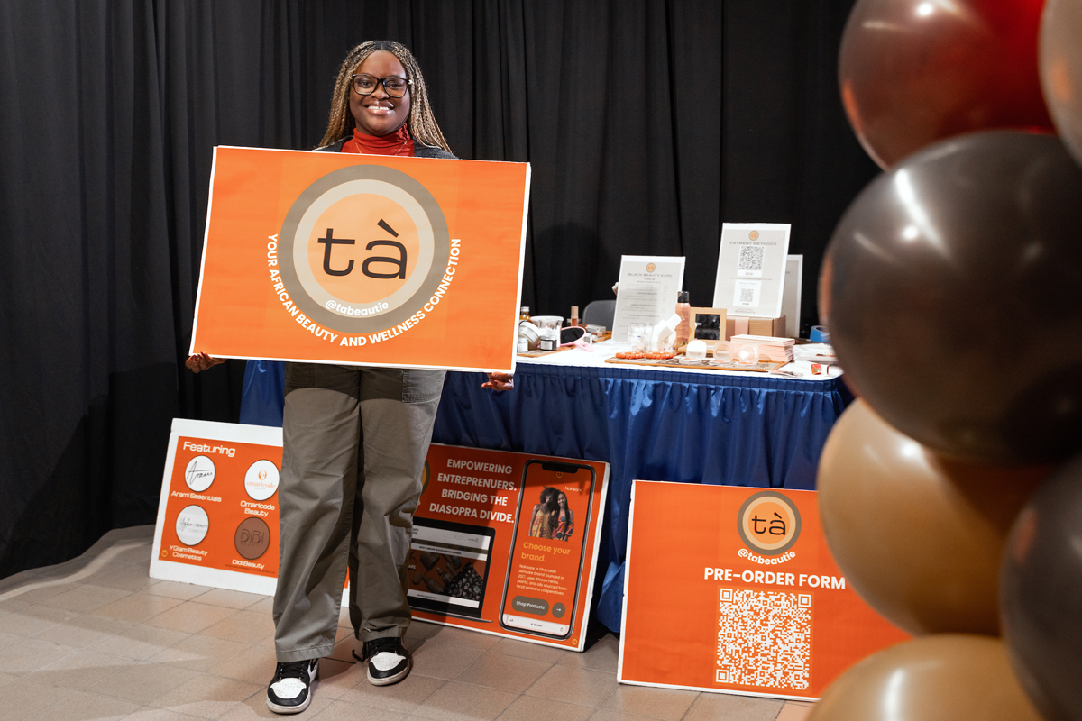 A student poses with a sign reading Ta, your African beauty and wellness connection.