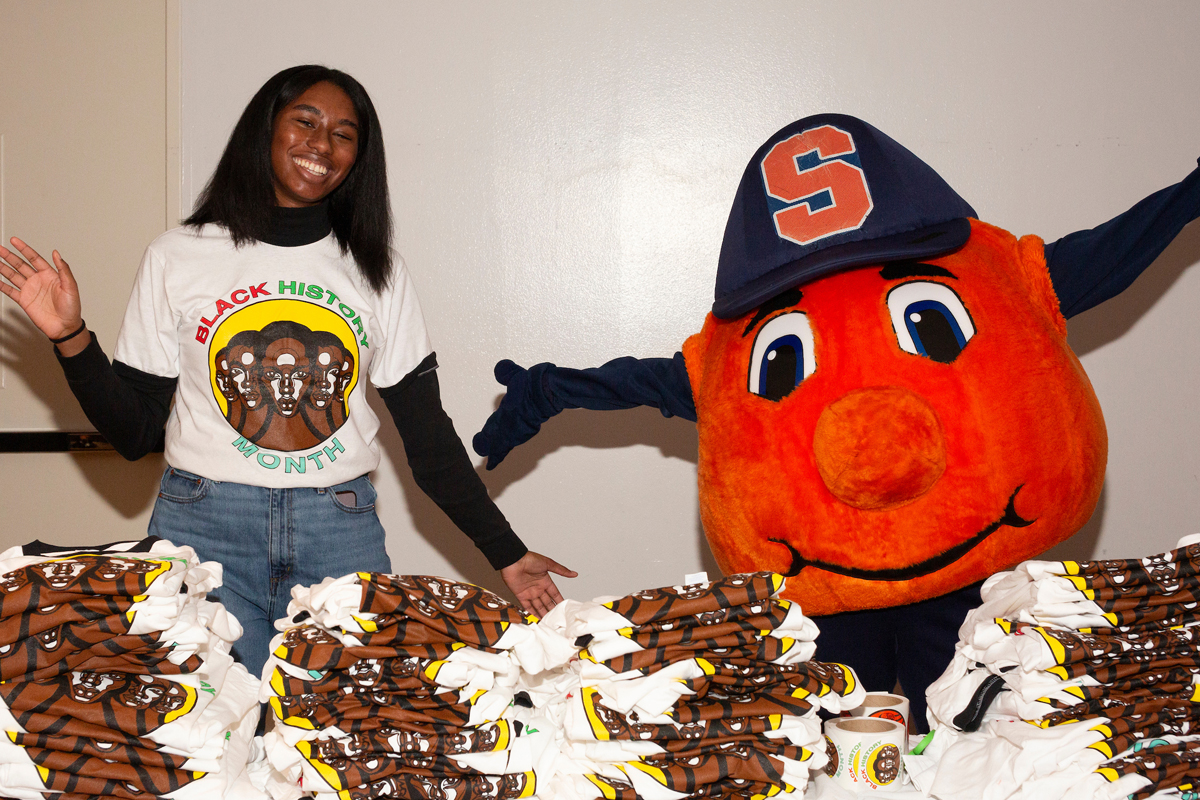 A student and Otto the Orange pose in front of the Black History Month t-shirts.