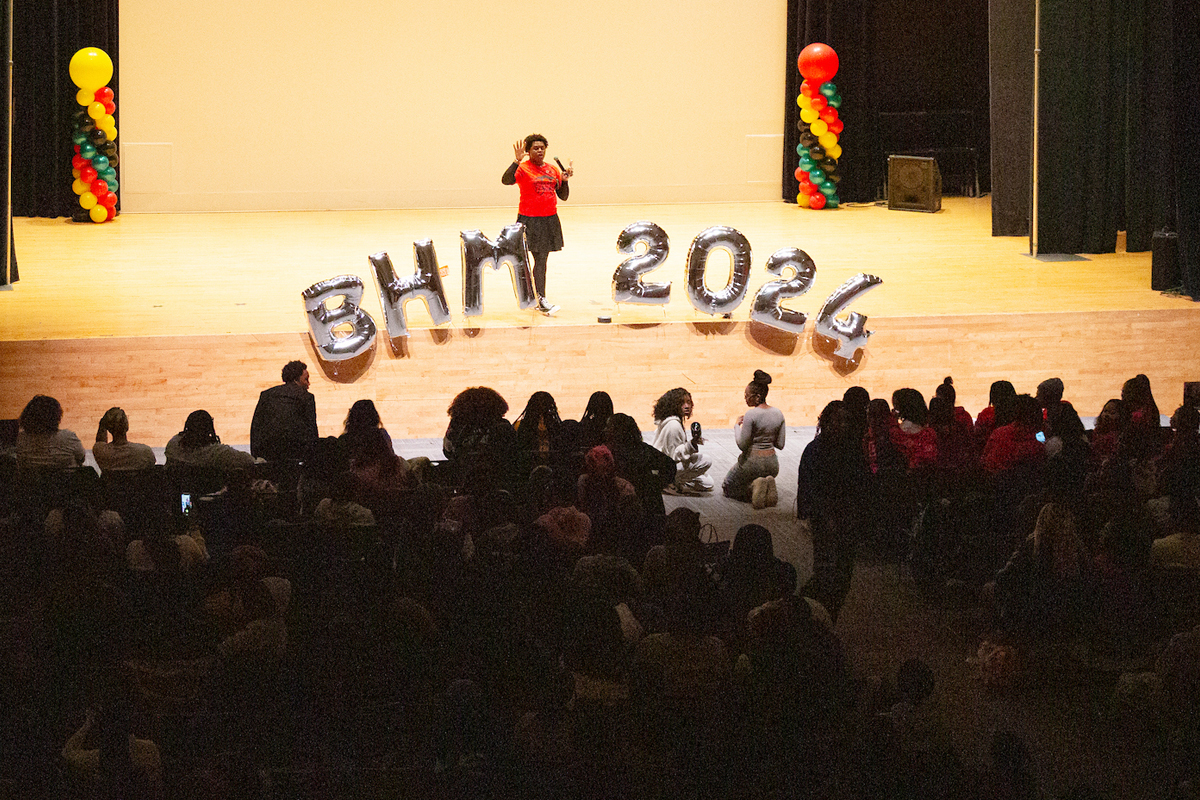 A person addresses the crowd. Balloons spelling out BHM 2024 rest on the stage.