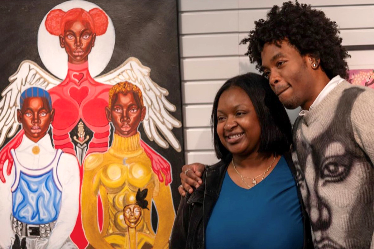 Two people pose for a photo next to an art display.