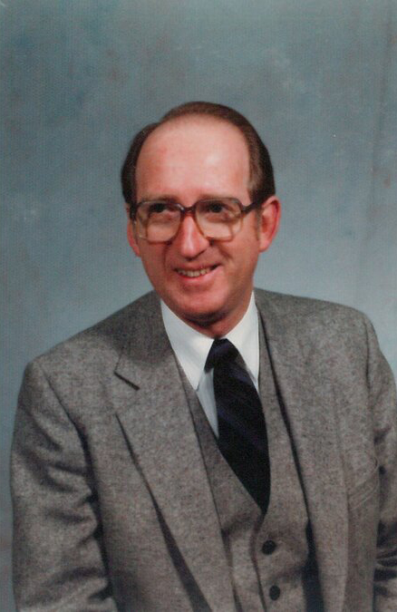 Person in a grey suit and black tie smiling against a grey gradient background.