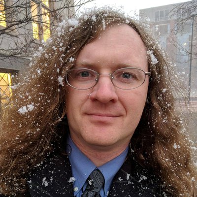 A man poses for a headshot while standing outside with snow in his hair.
