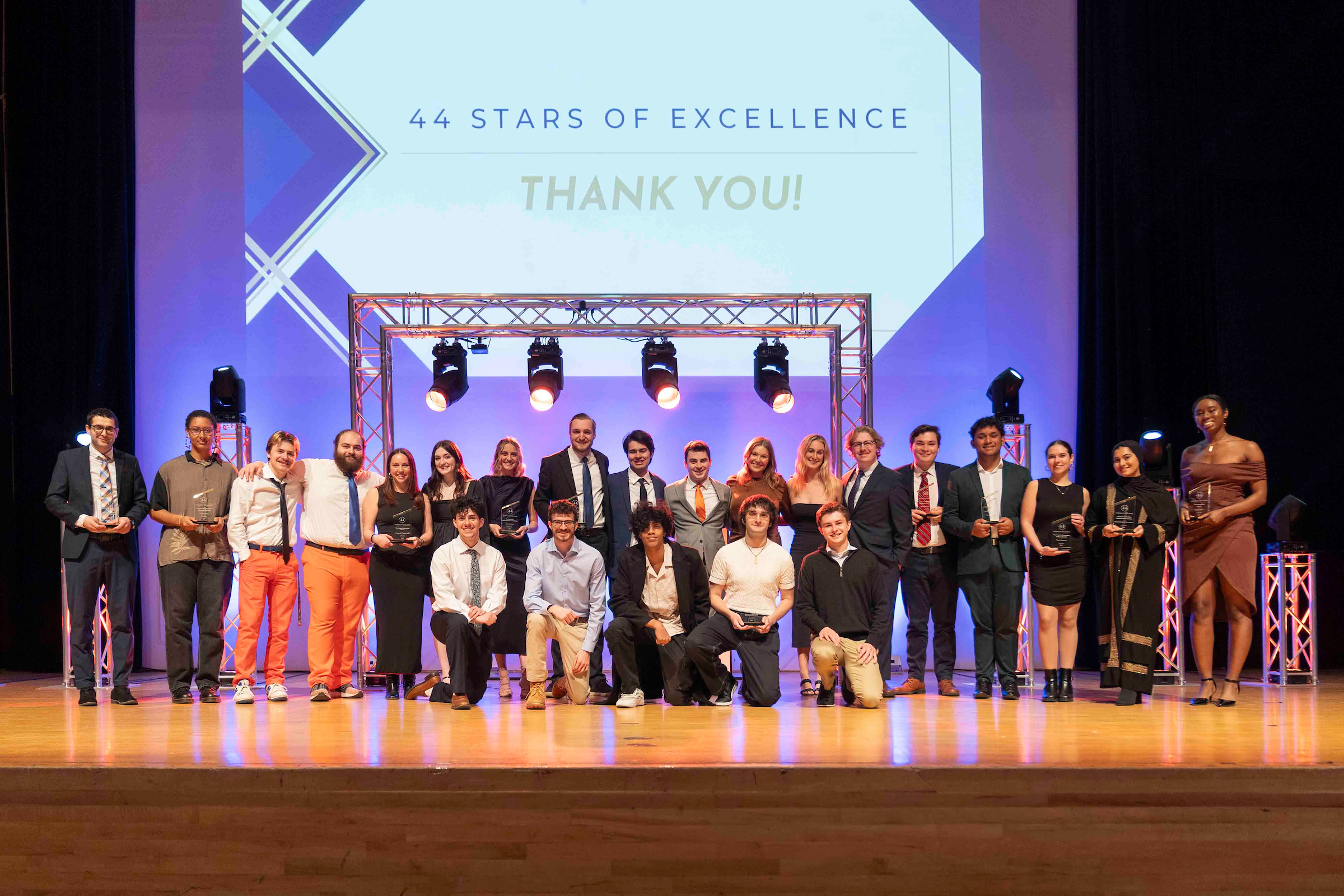 People standing on stage, some with awards, in front of a screen that says 44 Stars of Excellence, Thank you!