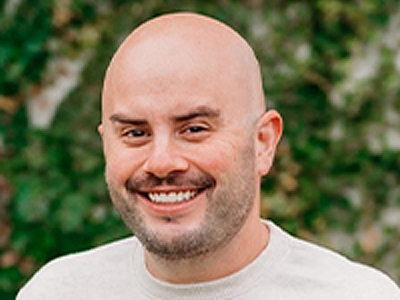 A man smiles while posing for a headshot outdoors.