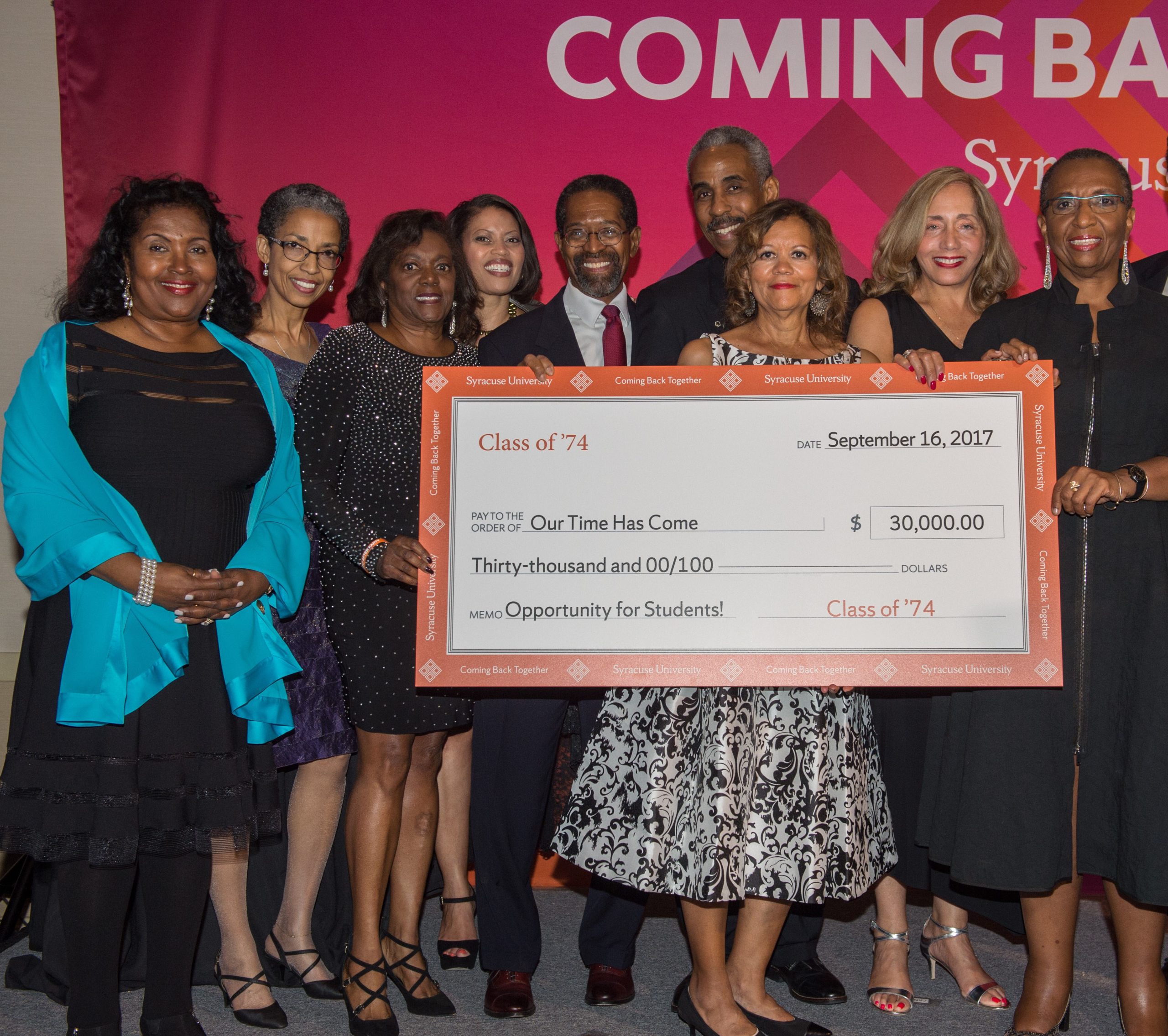 Large group of people standing together on a stage holding an oversized check