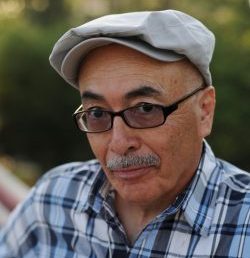 man with cap and plaid shirt and glasses looking at camera