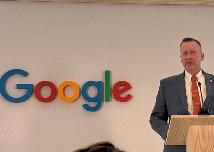 A man delivers remarks while standing at a podium. The Google logo is on the left portion of the background.