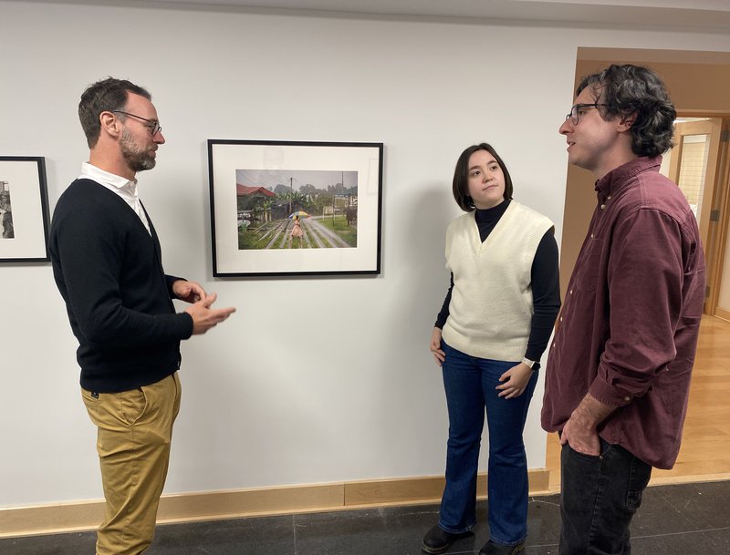 Three people standing in front of a framed picture on a wall talking.
