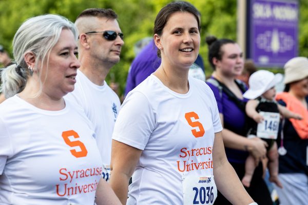 Two people in white T-shirts that say Syracuse University walking in a race.