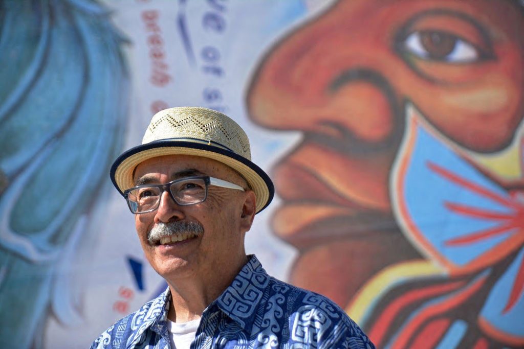 A poet stands outside of a mural painted on a wall.