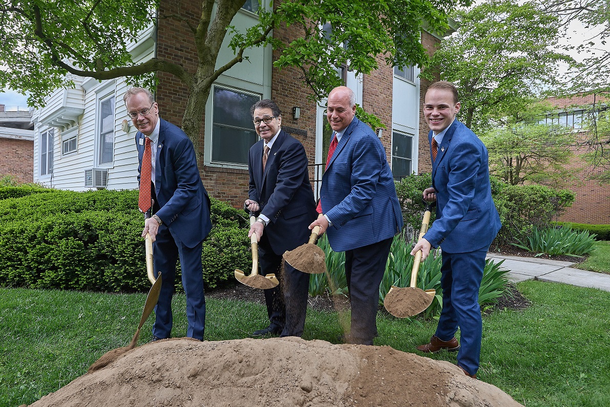 four people standing outside holding shovels with dirt