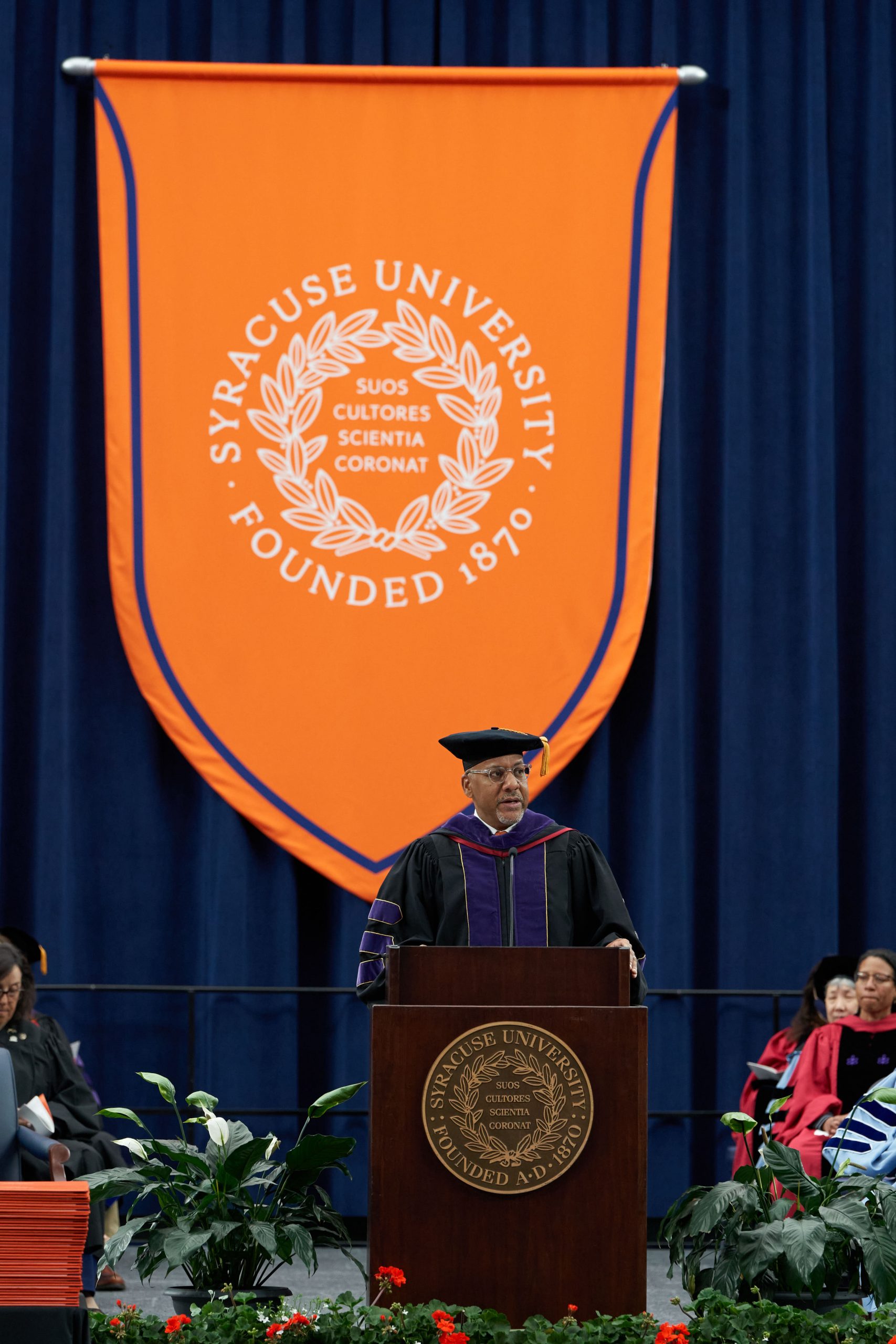 Person standing at a podium speaking on a stage at Commencement