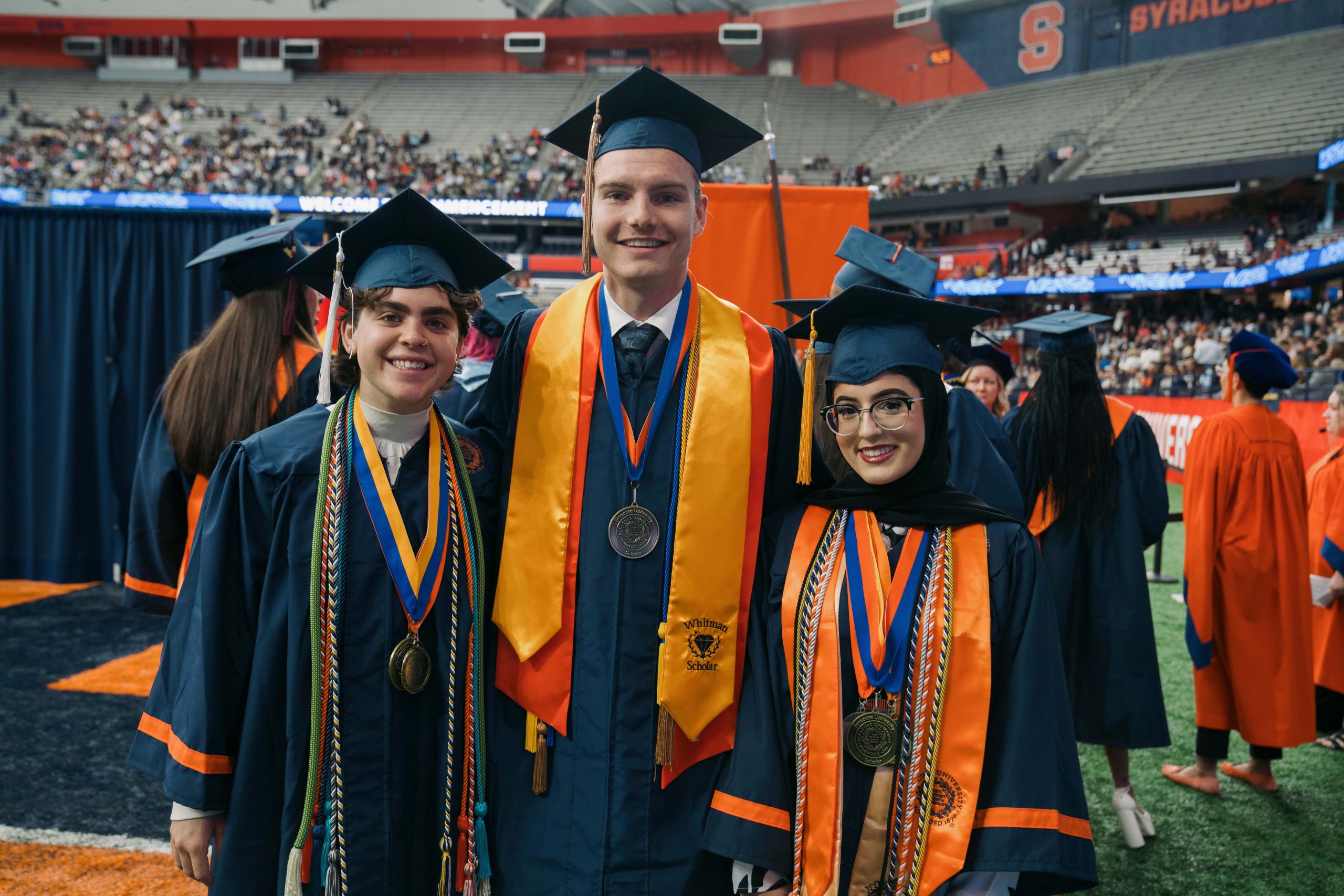 Three students standing together for a photo wearing caps and gowns.