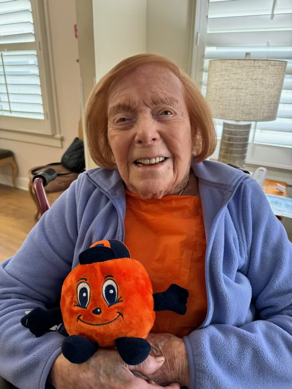 Woman sitting down smiling holding an Otto the Orange stuffed animal. 