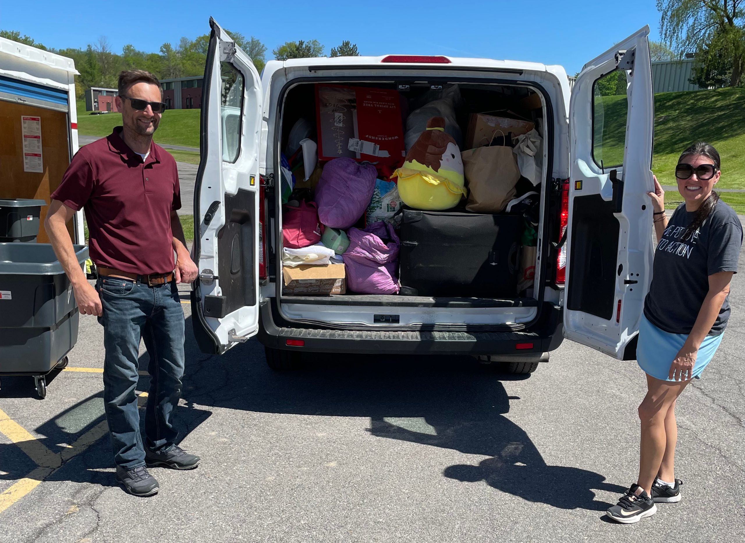 Two people standing outside either side of a full passenger van with items to be donated