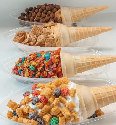 Four ice cream cones in dishes dipped in different types of cereal