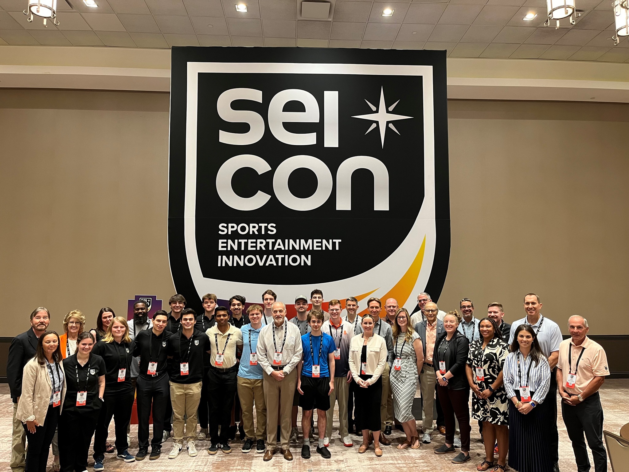 Large group of people standing in front of a banner that says SEI CON Sports Entertainment Innovation.