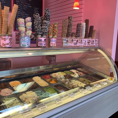 Large ice cream case full of different ice cream flavors with decorated ice cream cones on the top of the case