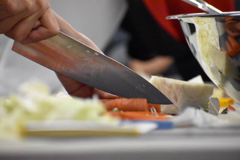 Hand holding a large knife white cutting carrots