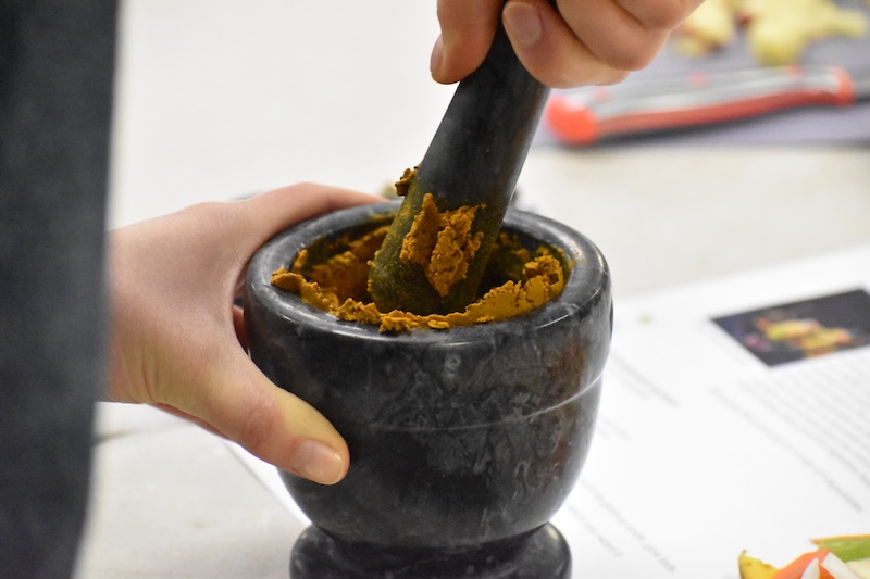 A person grouding together brown mustard seeds and turmeric powder using a mortar and pestle.