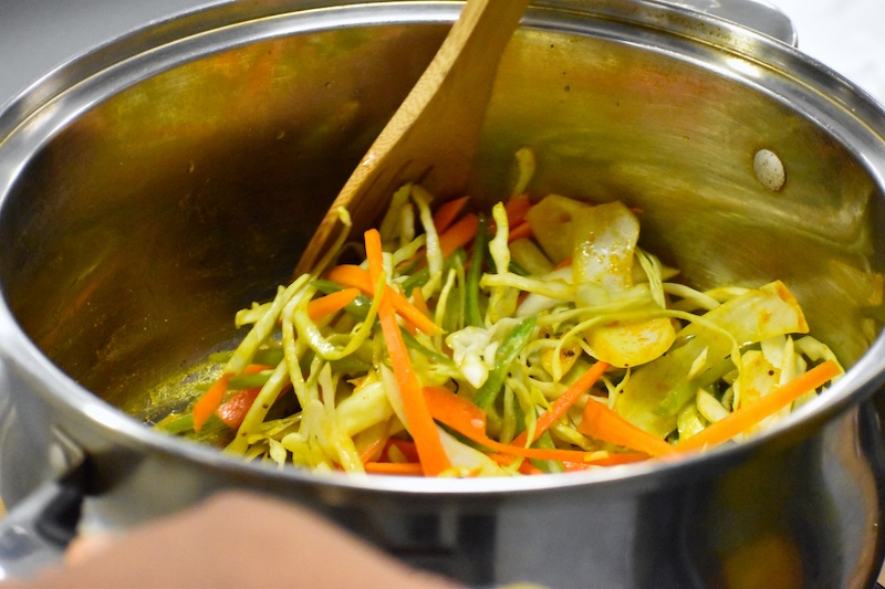 Someone mixing a pot full of mixed vegetables with a wooden spoon. 